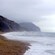 People walking along a sandy coastline between cliffs and ocean